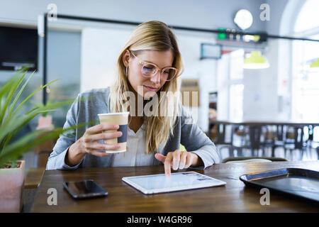 Giovane donna lavora con la sua tavoletta digitale mentre si beve il caffè nella caffetteria Foto Stock