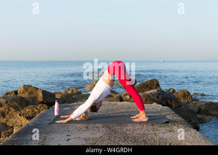 Giovane donna a praticare yoga sulla spiaggia, facendo del cane con la testa in giù Foto Stock