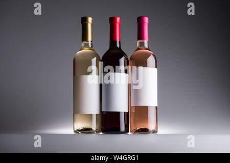Bottiglie di rosso, bianco e rosato con etichette in bianco su sfondo scuro con retro illuminazione Foto Stock
