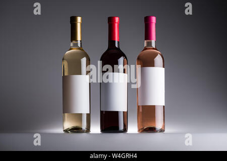 Bottiglie di bianco, rosso e rosato con etichette vuote su sfondo grigio Foto Stock