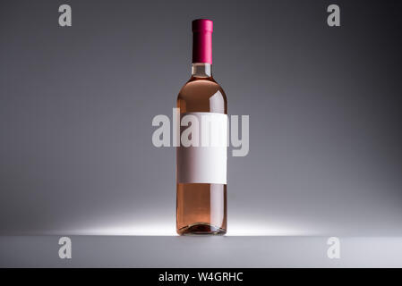 Bottiglia di vino rosato e etichetta in bianco su sfondo scuro con retro illuminazione Foto Stock