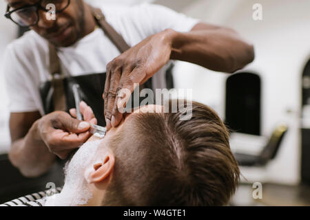 L'uomo ottenendo la sua barba rasata con il rasoio in un barbiere Foto Stock