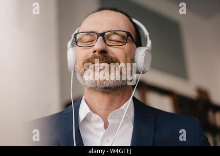 Imprenditore maturo con gli occhi chiusi per ascoltare musica con le cuffie Foto Stock