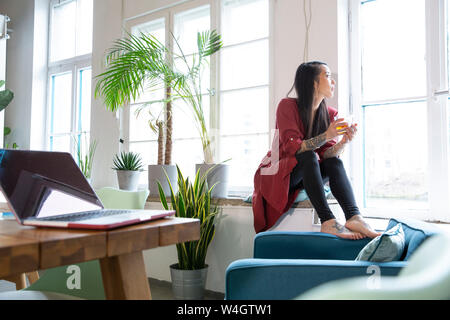 Donna che guarda fuori della finestra in ufficio Foto Stock