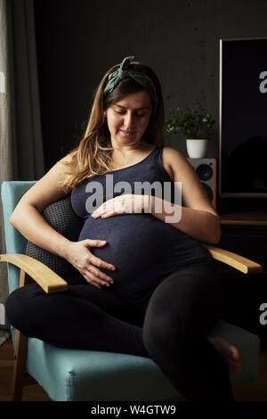 Donna incinta guardando sul suo ventre bambino a casa Foto Stock