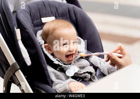 Alimentazione madre Laughing baby boy in passeggino Foto Stock