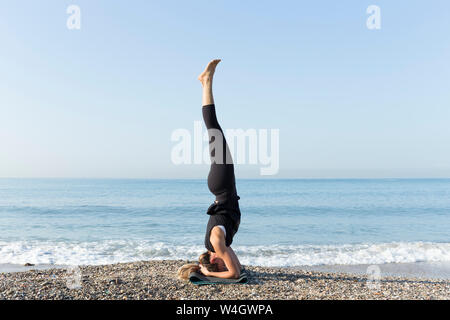 Giovane donna a praticare yoga sulla spiaggia, facendo headstand Foto Stock