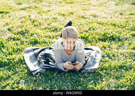 Giovane donna sdraiata su un prato utilizza lo smartphone Foto Stock