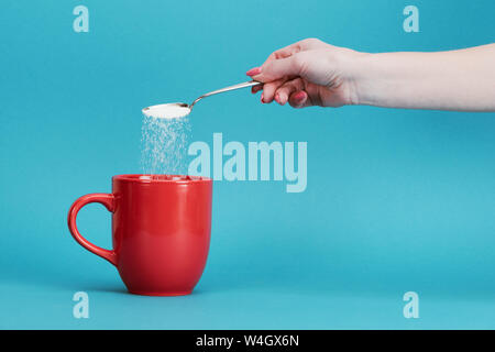Vista ritagliata della donna con aggiunta di zucchero nel bicchiere di rosso su sfondo blu Foto Stock