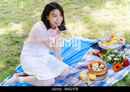 Donna rilassata mediante telefono cellulare e avente un picnic nel parco Foto Stock