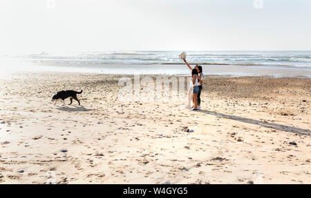 Tre donne con il cane a camminare sulla spiaggia Foto Stock