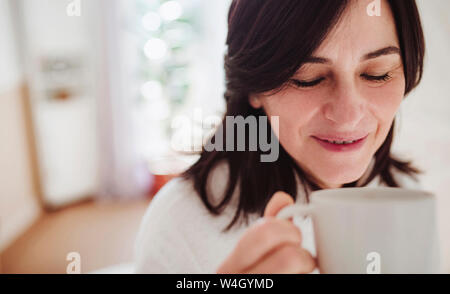 Donna matura in un bagno a casa gustando una tazza di caffè Foto Stock