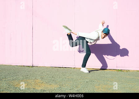 Giovane uomo di fronte rosa barriera di costruzione, in equilibrio su una gamba Foto Stock