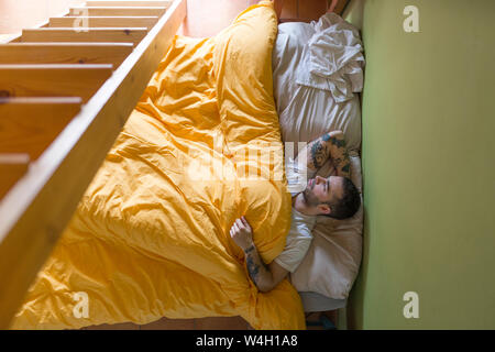 Tatuato uomo disteso nel letto, scaletta di legno Foto Stock