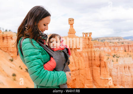 La donna che porta la figlia in un baby carrier a hoodoos nel Bryce Canyon dello Utah, Stati Uniti d'America Foto Stock