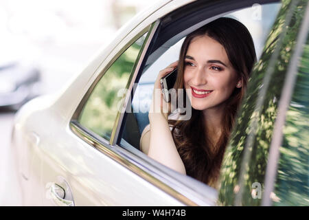 Una giovane ragazza è seduta sul sedile posteriore di un auto e sta parlando al telefono. Foto Stock