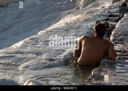 Turchia: uomini godendo il flusso di acqua dalle sorgenti calde sulle terrazze di travertino di Pamukkale (Castello di cotone), il sito naturale di sedimentar Foto Stock