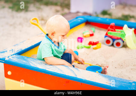 Carino baby boy giocare con giocattoli nel sandbox per esterno Foto Stock