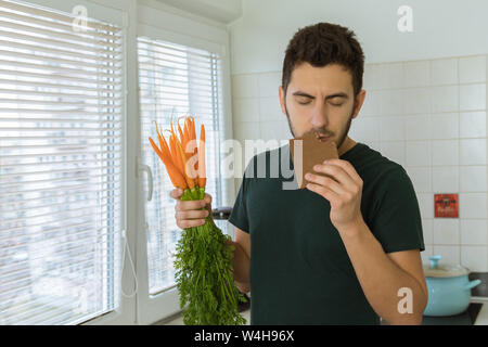 L'uomo mangia cioccolato con grande piacere. Egli non vuole mangiare le verdure. Foto Stock