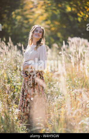 Sorridente bella donna incinta con gli occhi chiusi nel campo d'autunno. Foto Stock