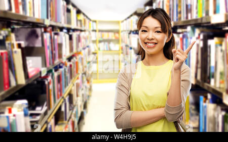 Felice donna asiatica puntare il dito fino in libreria Foto Stock