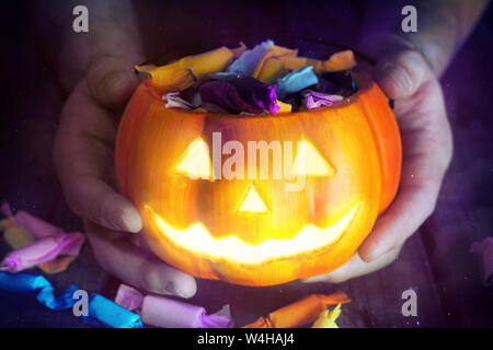 Tenere in mano la zucca incandescenza lampada richiesta di candy su sfondo scuro, retrò tema colore. Foto Stock