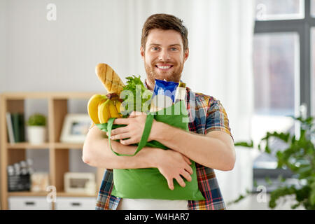 Sorridente giovane uomo con il cibo nel sacco a casa Foto Stock