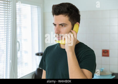 Una giovane bella bruna uomo sta parlando al telefono, invece di utilizzare una banana. Foto concettuale. Foto Stock