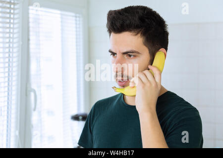 Una giovane bella bruna uomo sta parlando al telefono, invece di utilizzare una banana. Foto concettuale. Foto Stock