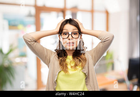 Donna asiatica in bicchieri tenendo la testa in ufficio Foto Stock