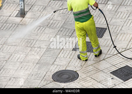 Lavoratore la pulizia del marciapiede di strada con il getto di acqua ad alta pressione. Pubblica il concetto di manutenzione Foto Stock