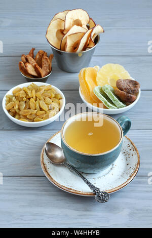 Dessert vegetariano: pezzi di canditi di ananas, kiwi e mango, di fichi secchi e di uva passa dorata, mela e pera chip in piccole ciotole e una tazza di te verde Foto Stock