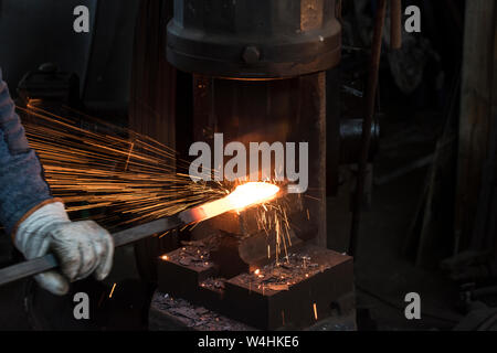 Fabbro forgiare rosso-metallo caldo con martello meccanico. Concetto blacksmithing. Foto Stock