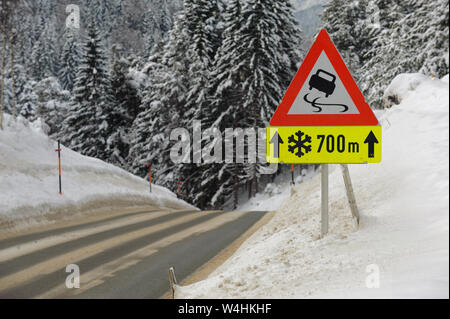 Segno di traffico sulla strada avverte di ghiaccio e di neve in inverno Foto Stock