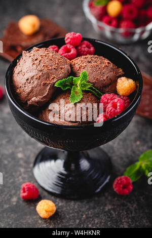 Tre brown di gelato al cioccolato sfere con lampone e foglie di Menta in vaso nero su sfondo scuro Foto Stock