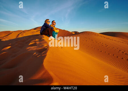 Turista giovane guardando sunrise nel deserto seduto su di una duna di sabbia in Marocco Sahara Africa Foto Stock