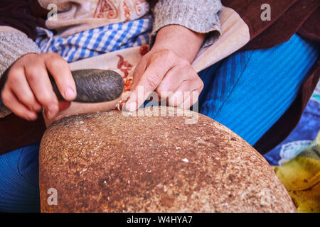 Una donna marocchina di cracking dadi argan con un utensile di pietra su pietra alla produzione artigianale di olio di argan per la cosmesi e per la preparazione di alimenti Foto Stock