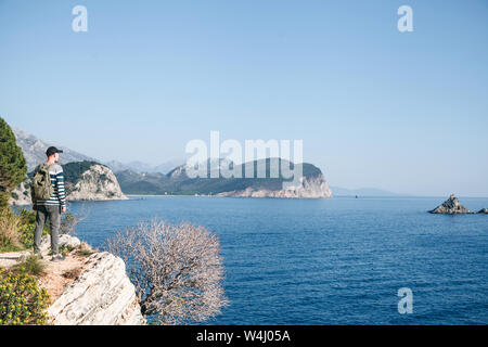 Un turista con lo zaino sulla cima di una scogliera o collina vicino al mare appare in lontananza. Viaggiare da soli. Foto Stock