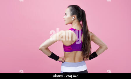 Un giovane attraente atletico brunette ragazza con una coda di cavallo in un luminoso stretto top dimostra il suo adorabile forma atletica con le mani sulla sua vita. Foto Stock