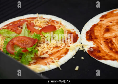 Tortilla pizza con formaggio, lattuga, pomodori. Servito molto caldo, dal grill. Concetto di cucina nazionale, sana il fast food Foto Stock