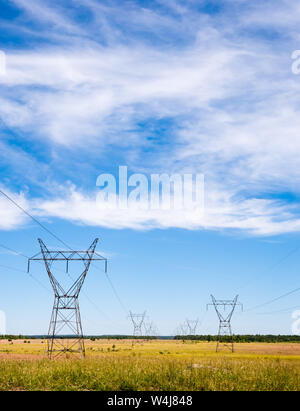 Elettrici grandi torri di trasmissione e linee di alimentazione rientranti nella distanza su campi rurali sotto parzialmente nuvoloso sky. Foto Stock