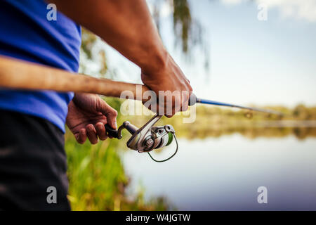 Giovane uomo di pesca sul fiume al tramonto. Primo piano della fiserman asta di supporto. Attrezzatura da pesca e vestiti. La Filatura Foto Stock