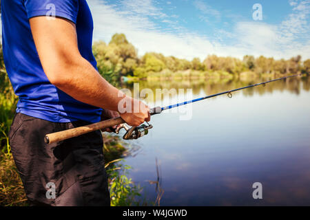 Giovane uomo di pesca sul fiume al tramonto. Primo piano della fiserman asta di supporto. Attrezzatura da pesca e vestiti. La Filatura Foto Stock