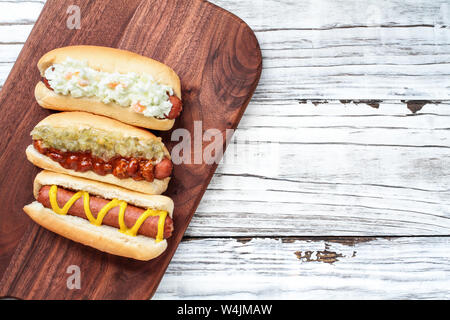 Tre varietà di hot dog su un tagliere. Uno con coleslaw, uno con sottaceti relish e il peperoncino e una pianura con uno solo di senape. Immagine ripresa Foto Stock