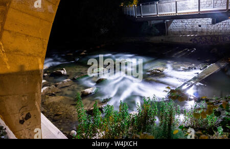 Una lunga esposizione cattura di un fiume in seguito su alcune rocce attraverso un ponte Foto Stock