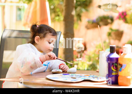 Carino bambina divertendosi, la colorazione con pennello, Scrittura e pittura. Preschooler bambino con vernice a giardino d'autunno. Bambini disegno su una pietra. Presch Foto Stock