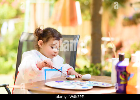 Carino bambina divertendosi, la colorazione con pennello, Scrittura e pittura. Preschooler bambino con vernice a giardino d'autunno. Bambini disegno su una pietra. Presch Foto Stock