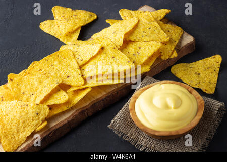 Nachos chips su legno scheda rustico con salsa al formaggio su sfondo scuro Foto Stock