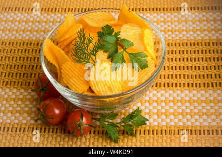 Natural Croccanti patatine fritte in un recipiente trasparente e decorate con foglie di aneto e prezzemolo. Vicino il vaso si trovano tre pomodori ciliegia. Il vaso si erge Foto Stock