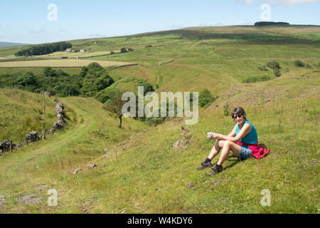 Attraente donna più anziana in appoggio durante una passeggiata sopra Westgate, nel North Pennines, Weardale, Co. Durham, England, Regno Unito Foto Stock